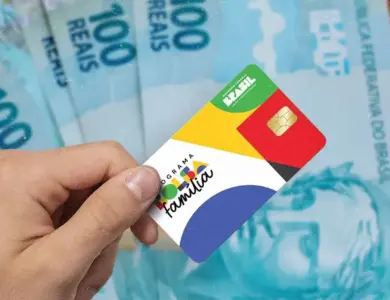 Cartão do Bolsa Família segurado por uma pessoa, com notas de real ao fundo, representando o pagamento antecipado do benefício em cidades de Minas Gerais.