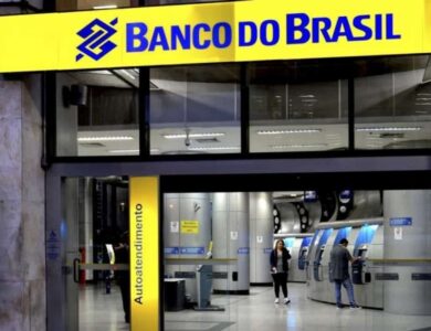 Pessoas utilizando caixas eletrônicos em agência do Banco do Brasil iluminada à noite