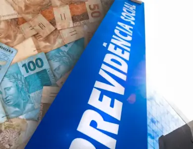 Notas de 50 e 100 reais sobrepostas ao lado de placa azul da Previdência Social com prédio ao fundo.