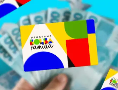 Mão segurando cartão colorido do Programa Bolsa Família sobre notas de reais desfocadas.