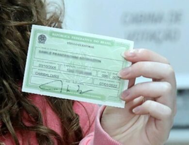 Mulher de cabelos castanhos cacheados segura título eleitoral verde da República Federativa do Brasil.